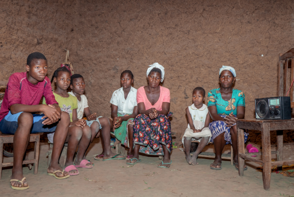 Camila with her 5 siblings and mother sitting in their mud house.
